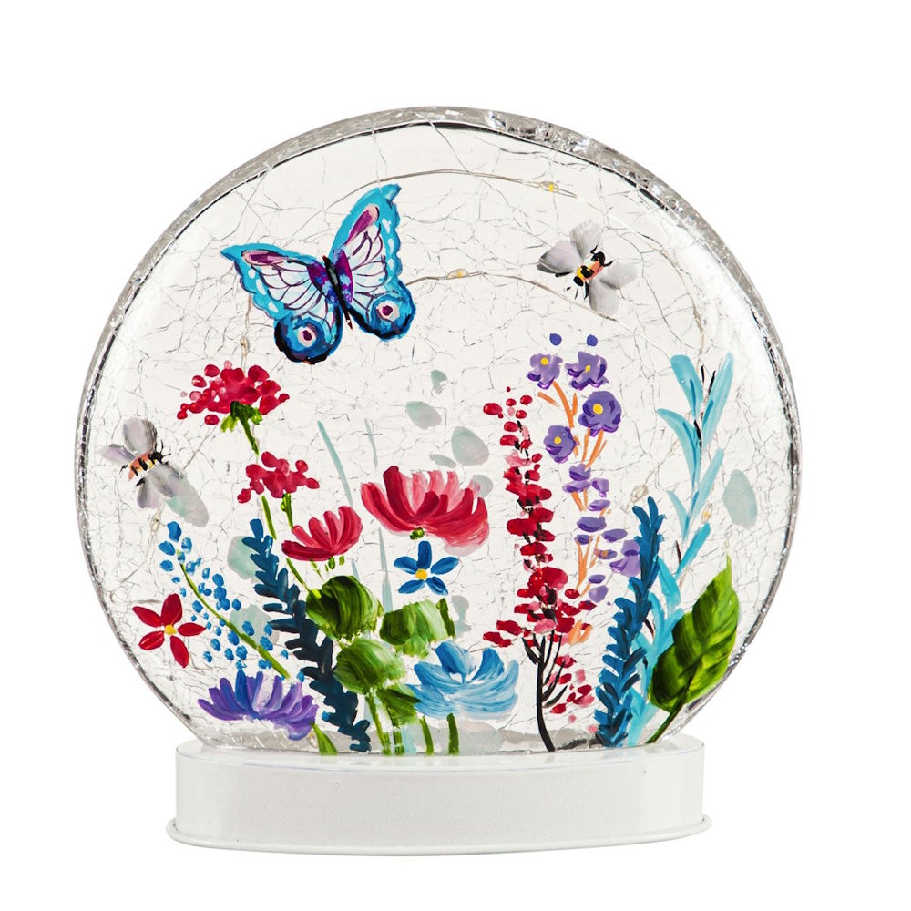 A round crackled glass disc on a white base, painted with colorful spring flowers and a blue butterfly.
