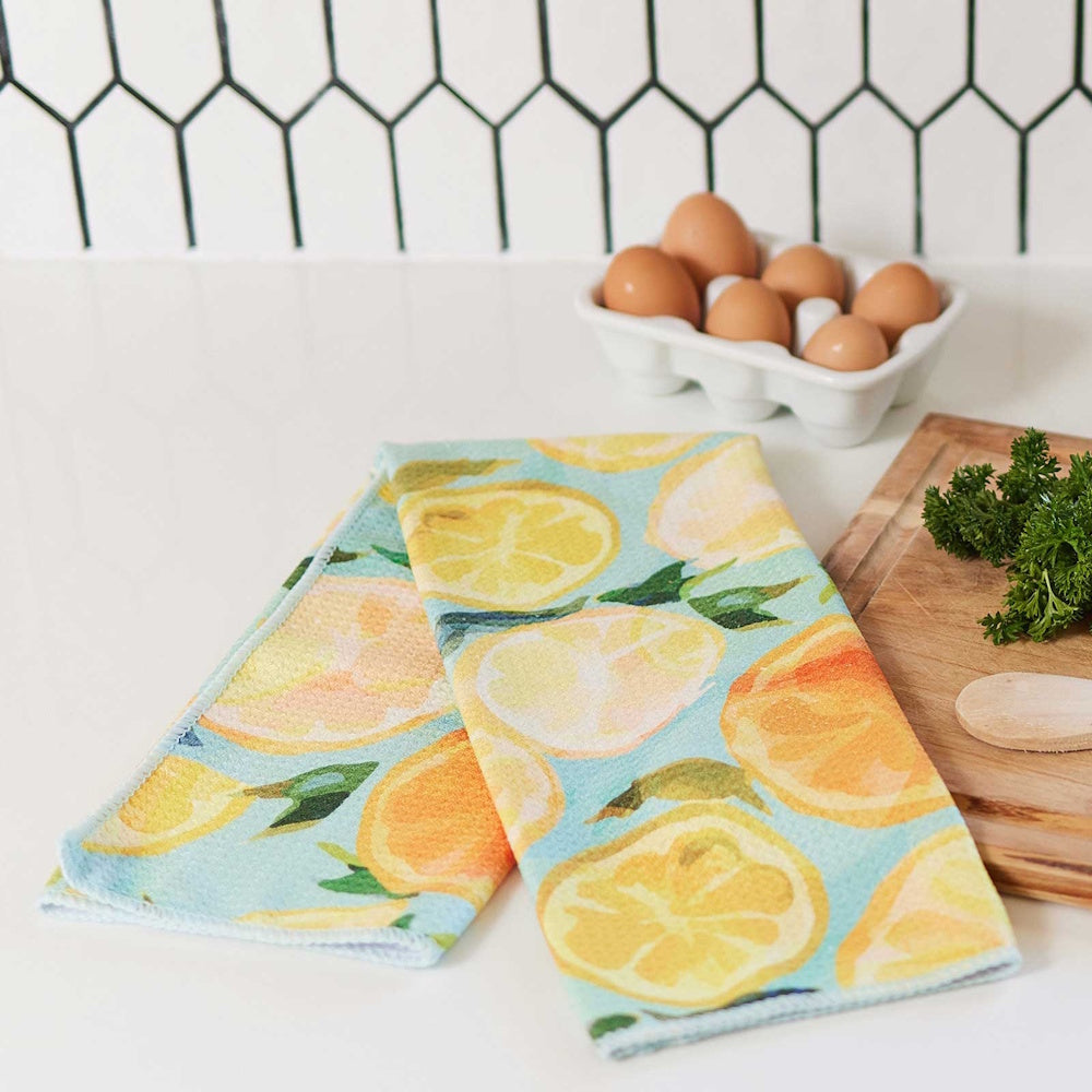 Lemon slice pattern kitchen tea towel displayed on a counter with eggs and a wooden cutting board in a bright kitchen.