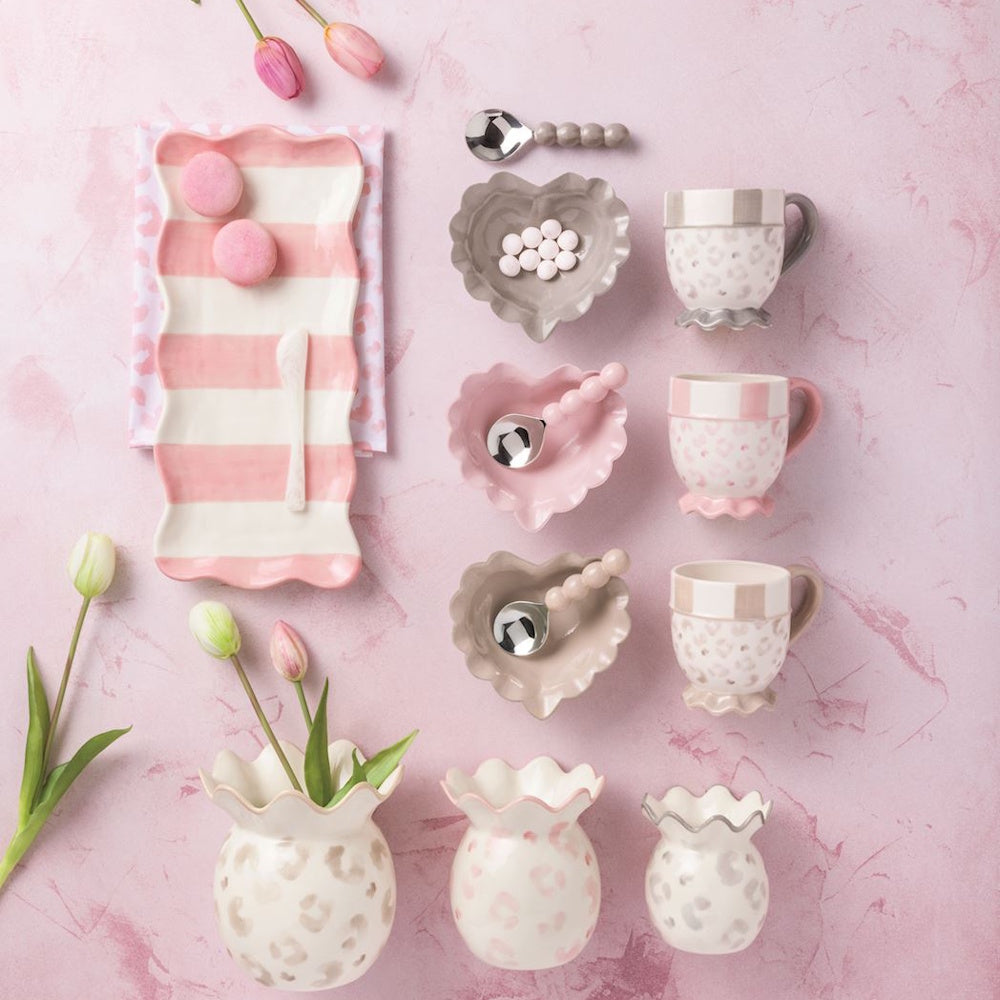 Pink and tan leopard print tea set with heart-shaped bowls, striped tray, and scalloped vases on a pink background.