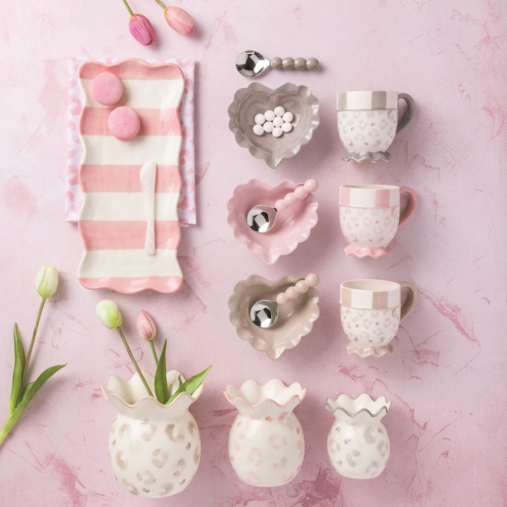 Leopard print ceramic vases and mugs with heart-shaped bowls and pink striped tray on a pink background.