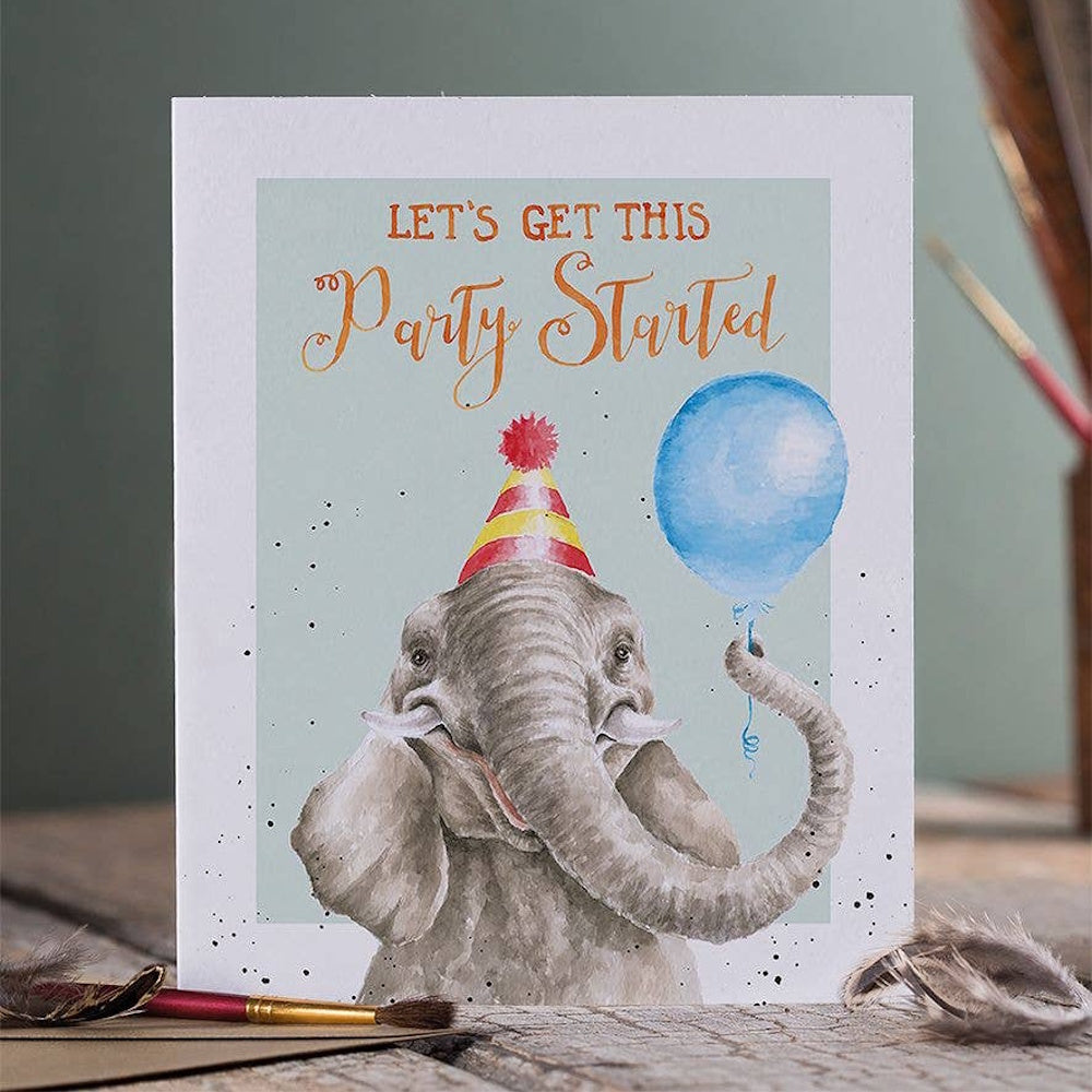 Watercolor illustration of a celebratory elephant wearing a party hat and holding a blue balloon with its trunk.