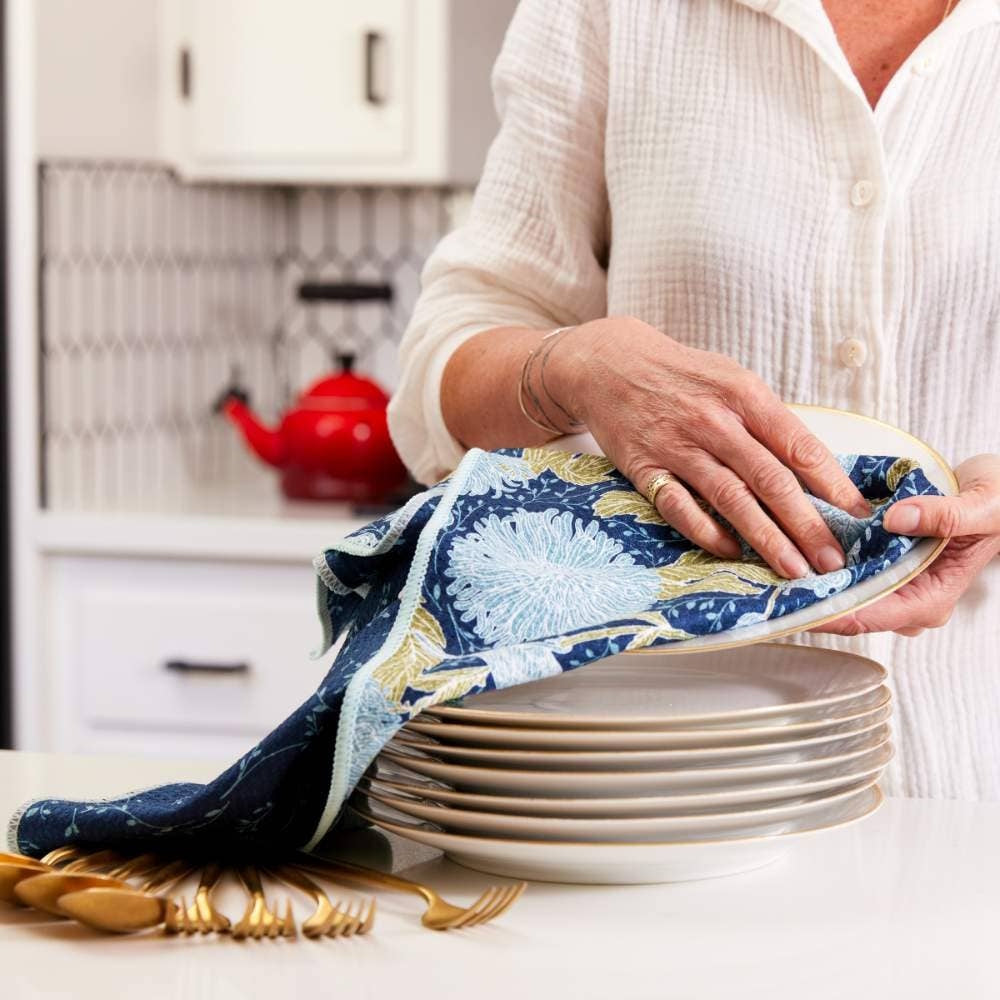 Woman drying a stack of white plates with a floral chrysanthemum and bird print eco-friendly kitchen tea towel.
