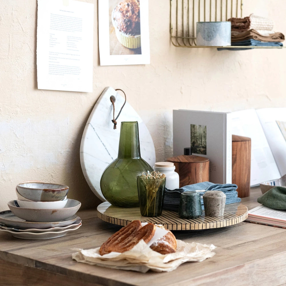 A teardrop-shaped white marble cheese board with a leather tie, leaning against a wall in a styled kitchen scene.