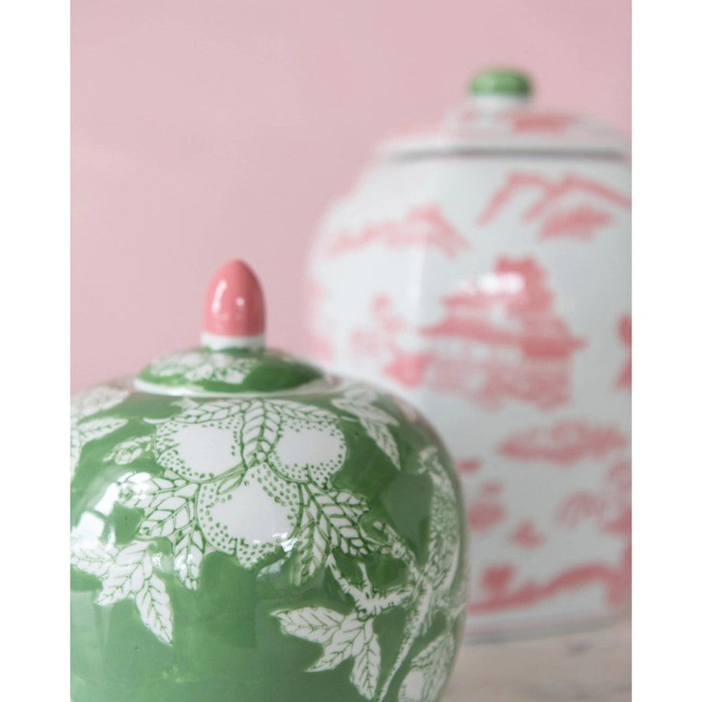 Green stoneware ginger jar with white floral pattern and pink finial against a blurred pink background.