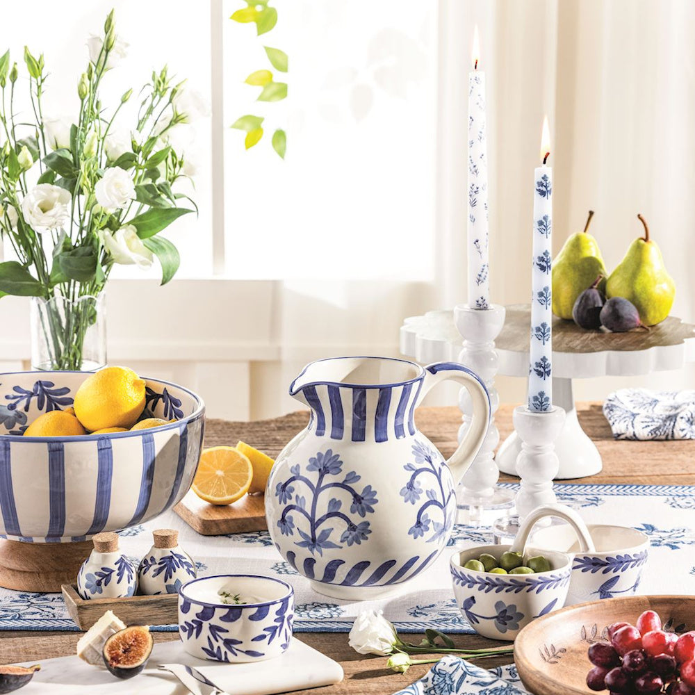 Blue and white patterned ceramic pitcher and bowls on a dining table with taper candles, lemons, and fresh fruit.