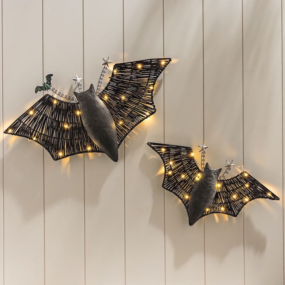 Two black lighted woven bat decorations hanging on a light paneled wall.