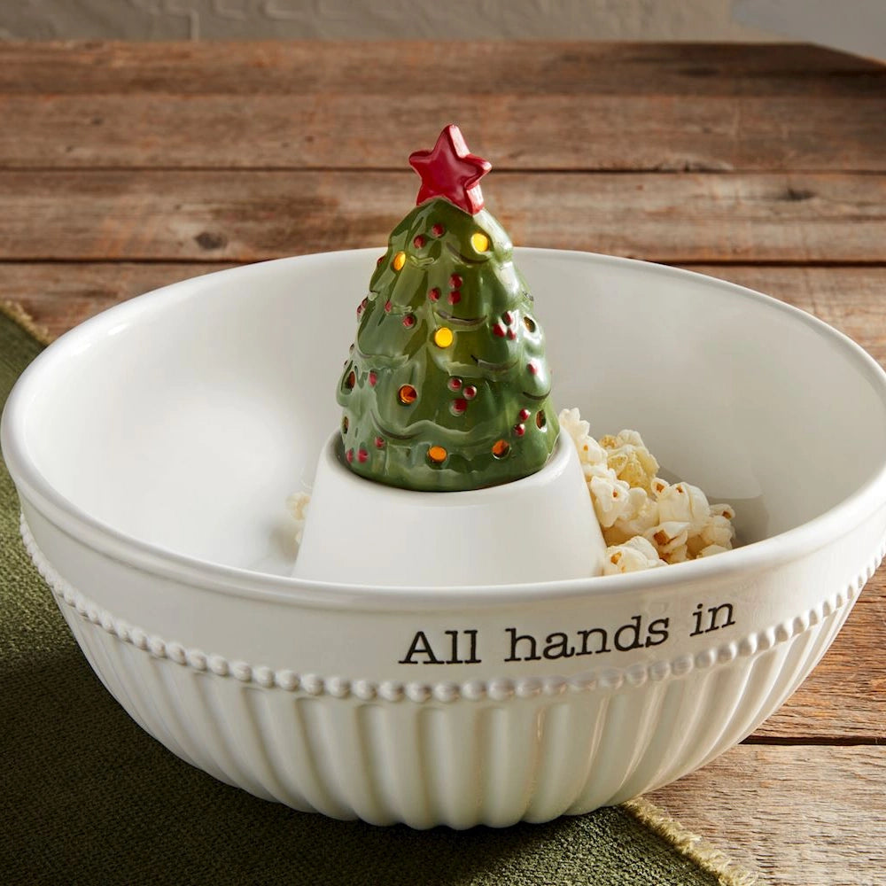 Lit ceramic Christmas tree sitter placed inside a white ceramic snack bowl reading "All hands in".