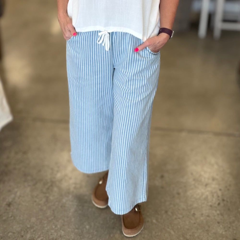 Woman wearing light blue and white striped wide-leg cropped pants with drawstring waist.