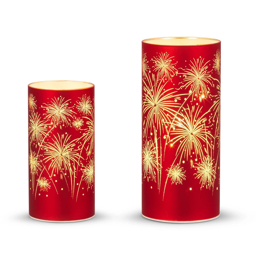 Two red candles with gold firework patterns glow warmly against a white background. The taller candle is on the right, adding a festive, celebratory feel.