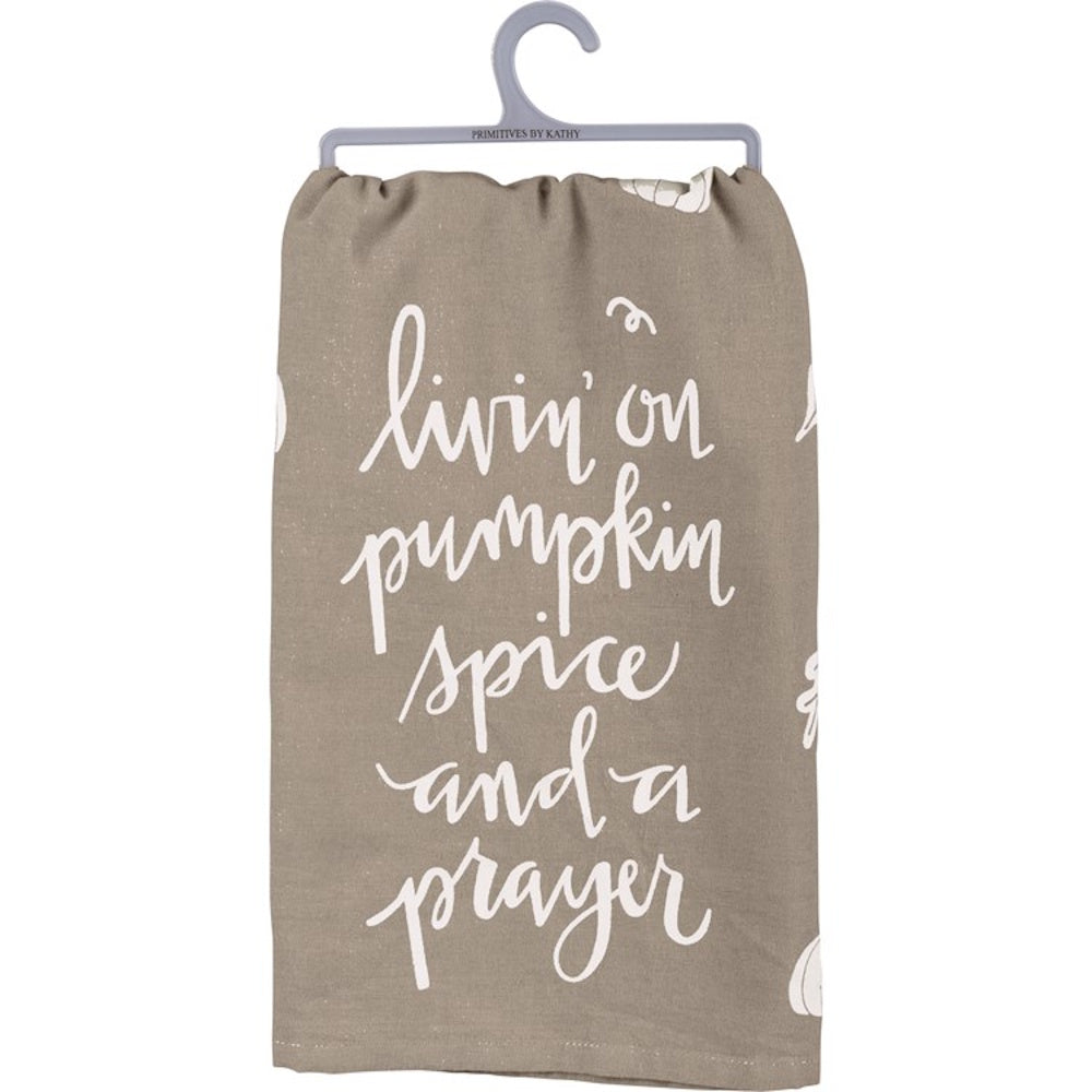 A taupe kitchen towel with white script text reading "livin' on pumpkin spice and a prayer."