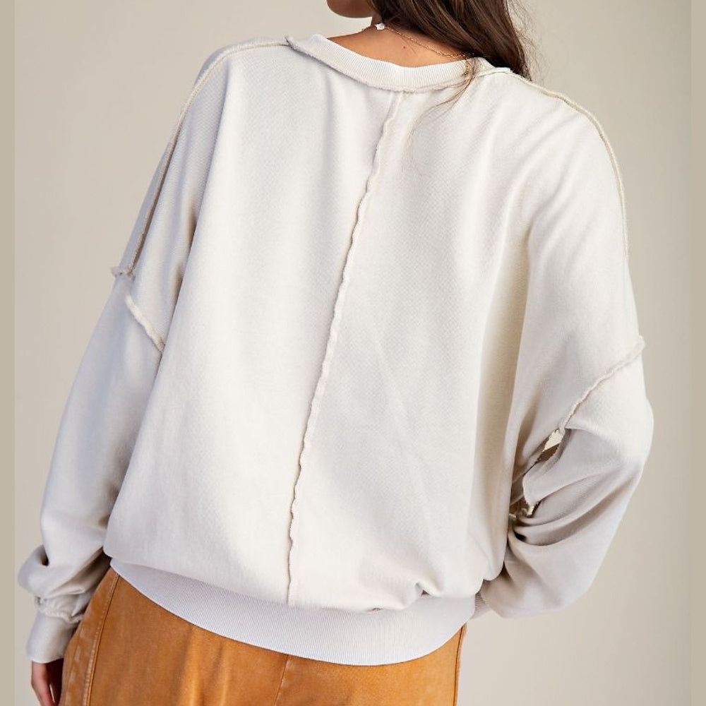 Back view of a woman in a cream mineral-washed long-sleeve pullover with exposed seam detailing and ribbed hem.