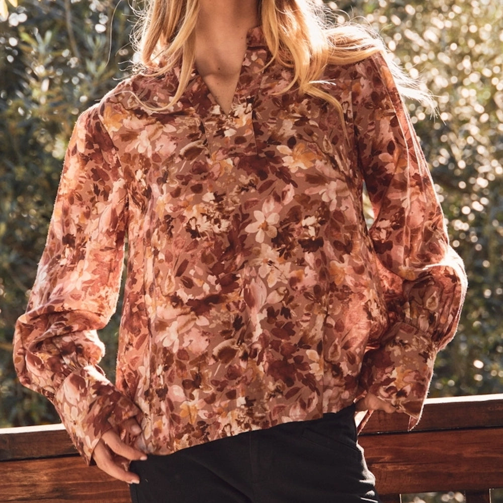 Woman wearing a long-sleeve floral blouse in warm earth tones with a split neckline.