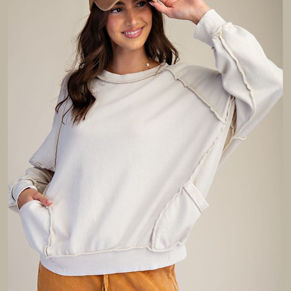 Cream mineral-washed long-sleeve pullover with raw edge seam detailing and side pockets.