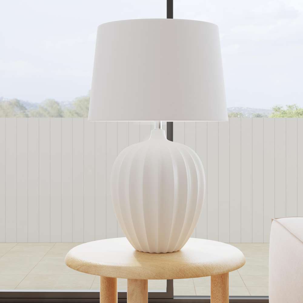 Modern white ribbed ceramic table lamp with fabric drum shade on a wooden side table.