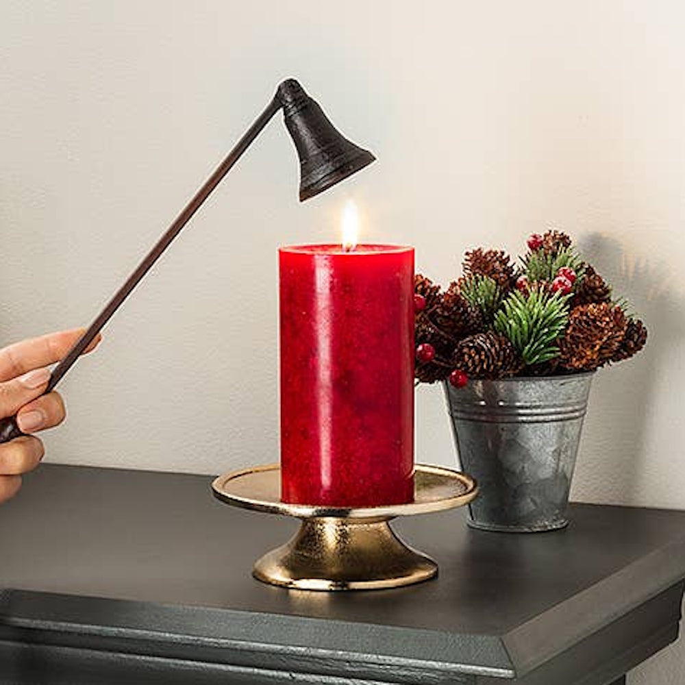 Hand holding a metal snuffer over a lit red candle on a gold pedestal plate.
