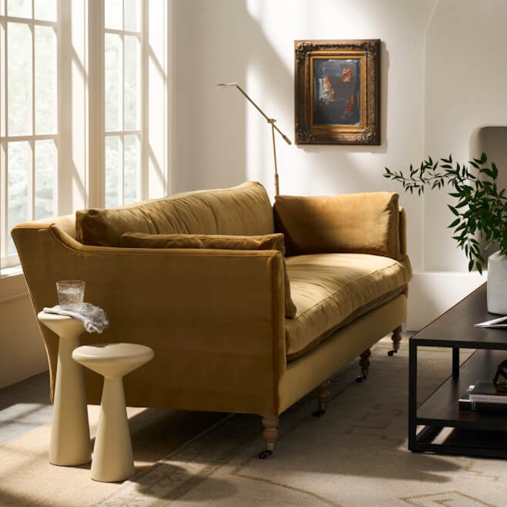 Antiqued amber velvet sofa in a sunlit living room with modern side tables and a classic framed painting.