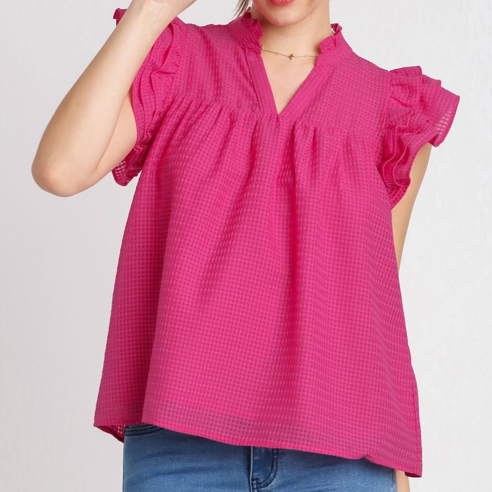 A woman wearing a vibrant magenta, textured split-neck top with layered ruffle cap sleeves and a loose fit.