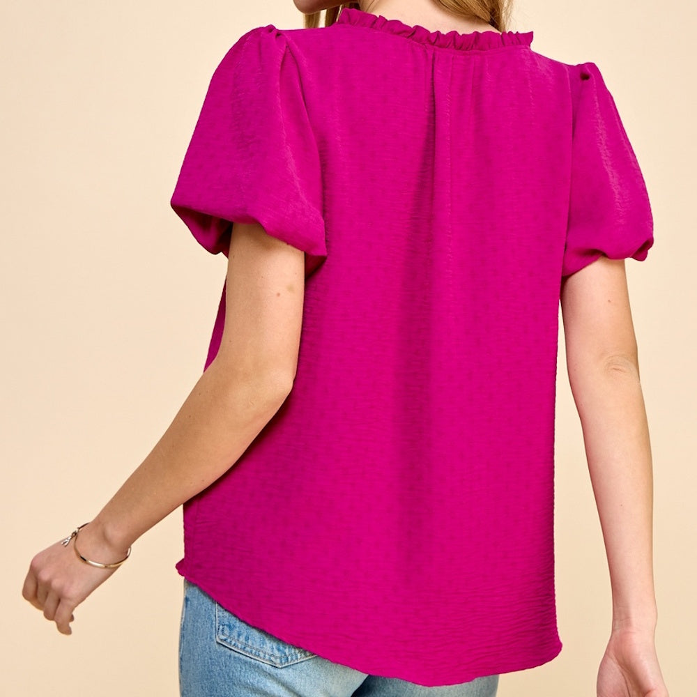 Rear view of a woman wearing a magenta, textured short-sleeve blouse with a ruffled collar and puff sleeves.