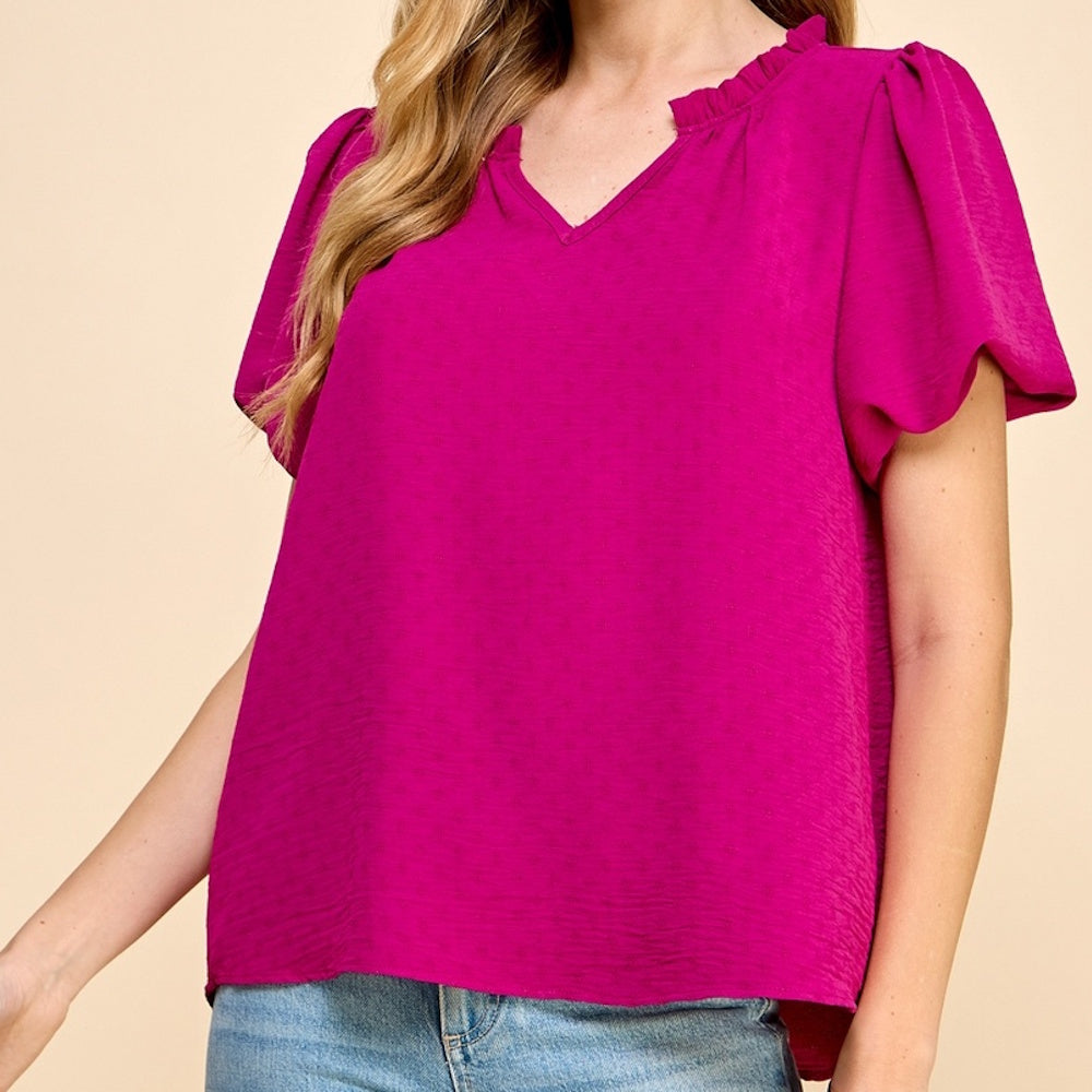 Side view of a person wearing a textured magenta blouse with short puff sleeves and a ruffled V-neckline.