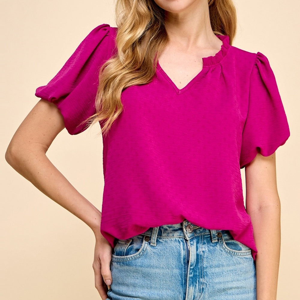 Woman wearing a textured magenta v-neck top with puff short sleeves and blue jeans.