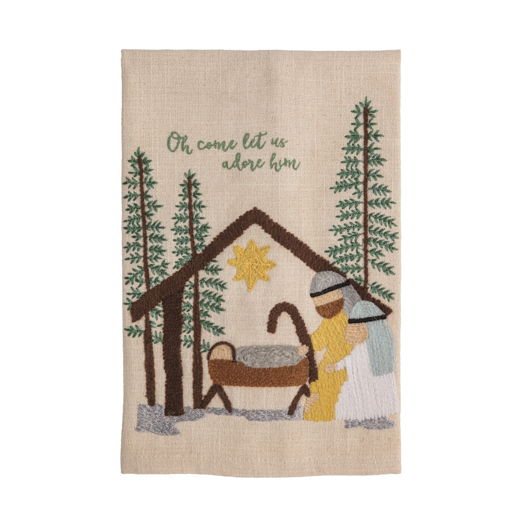 A beige embroidered towel featuring a manger scene, pine trees, and text reading "Oh come let us adore him".
