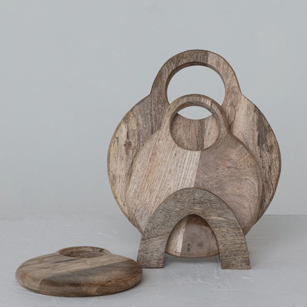 Round mango wood cutting boards with circular handles stacked in a matching wooden stand.