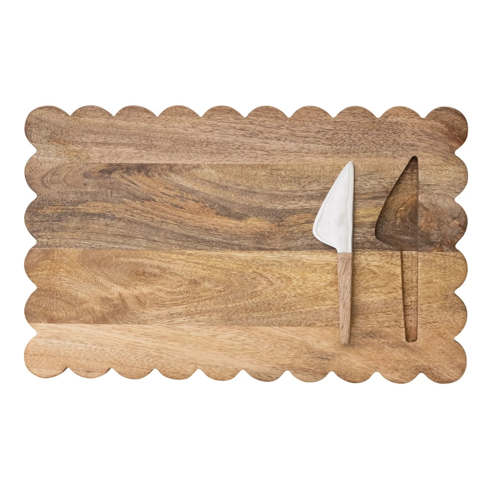 Scalloped edge wooden cheese board set with white marble and wood handled spreader knife on white background.