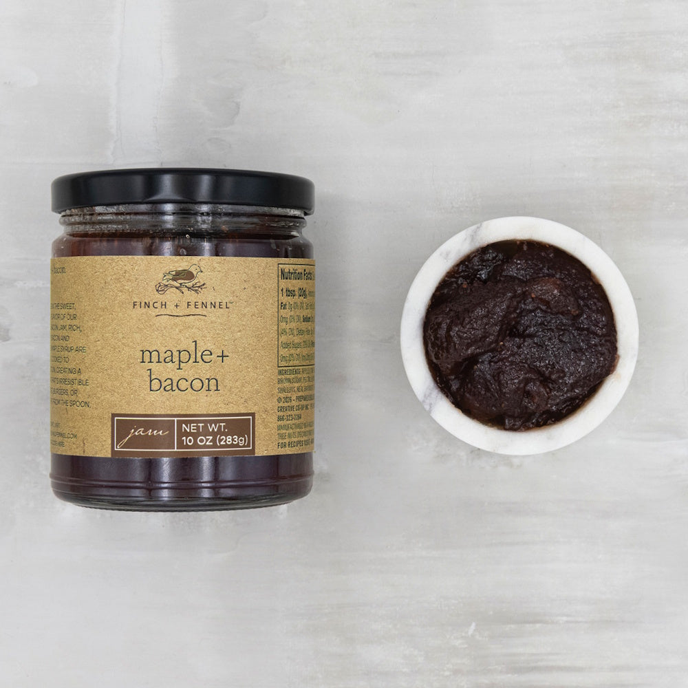 A jar of Finch & Fennel maple bacon jam next to a small marble bowl of dark jam, top-down view.