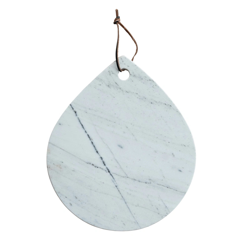 A simple, drop-shaped white marble serving board with a single brown leather cord hanging from its top.