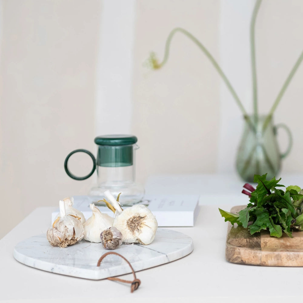Fresh garlic bulbs on a teardrop-shaped white marble cheese board in a bright, modern kitchen setting.