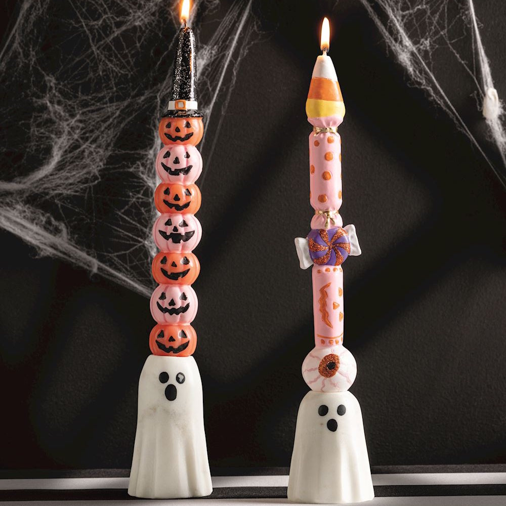 Two white ghost taper candle holders with lit, decorative Halloween candles set against a dark backdrop.