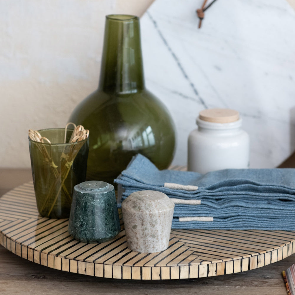 Green and beige marble salt and pepper shakers on a striped wooden tray with blue napkins and glassware.