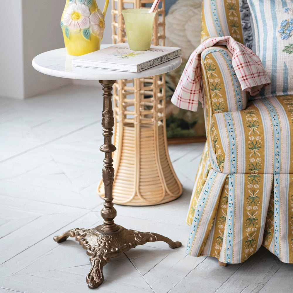 Round marble top side table with an ornate cast iron base, styled next to an armchair.