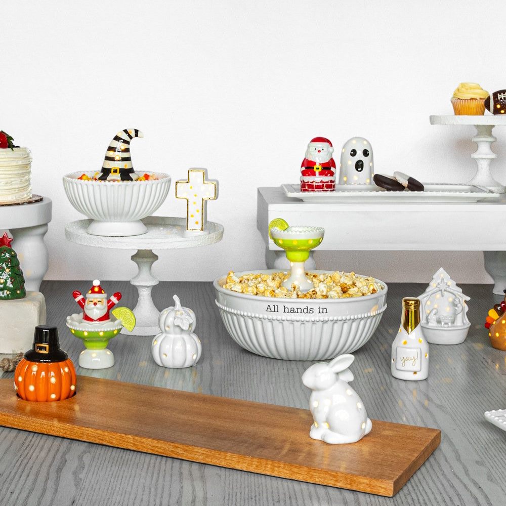 Assorted holiday-themed light-up ceramic figurines and bowls, including a pumpkin, bunny, Santa, and ghost on a table.