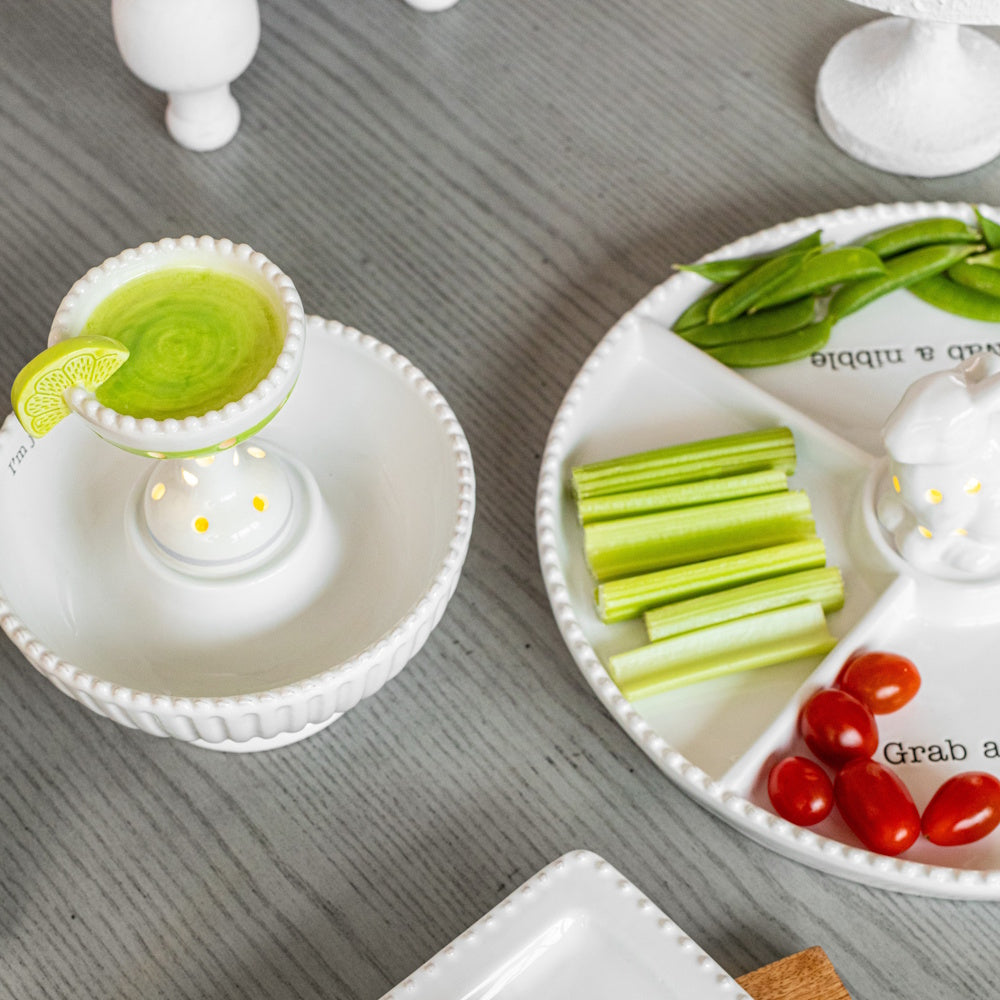 Ceramic margarita light-up sitter in a beaded white bowl next to a divided serving tray with fresh vegetables and snacks.
