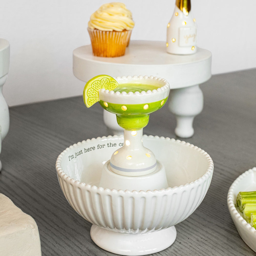 Ceramic light-up margarita sitter in a white beaded candy bowl on a gray table with a cupcake and party decor background.