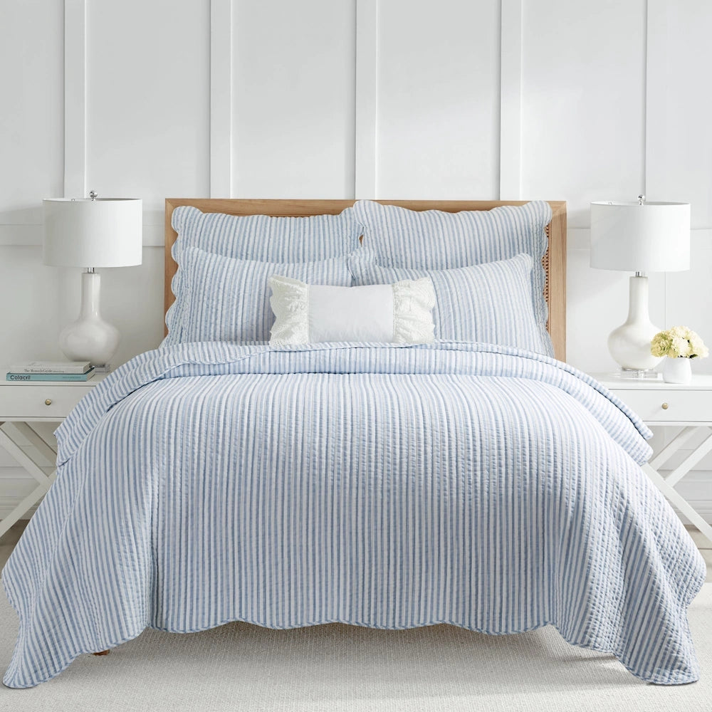 Light blue and white striped quilt set with scalloped edges on a bed framed by matching nightstands.