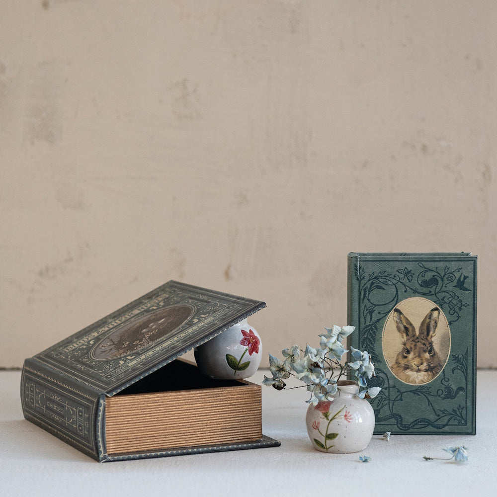 Two decorative book boxes, one featuring a rabbit illustration, next to a small floral vase.