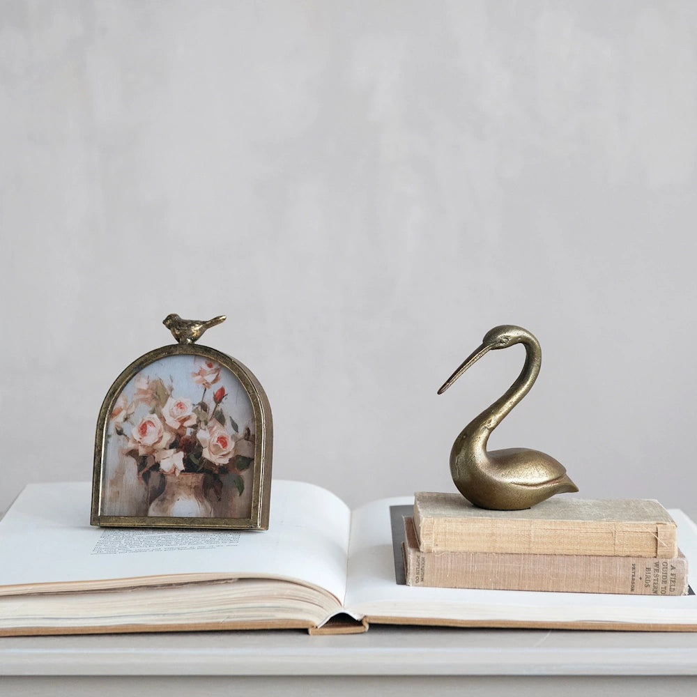 Antique gold arched bird photo frame with rose painting and brass swan figurine on vintage books.