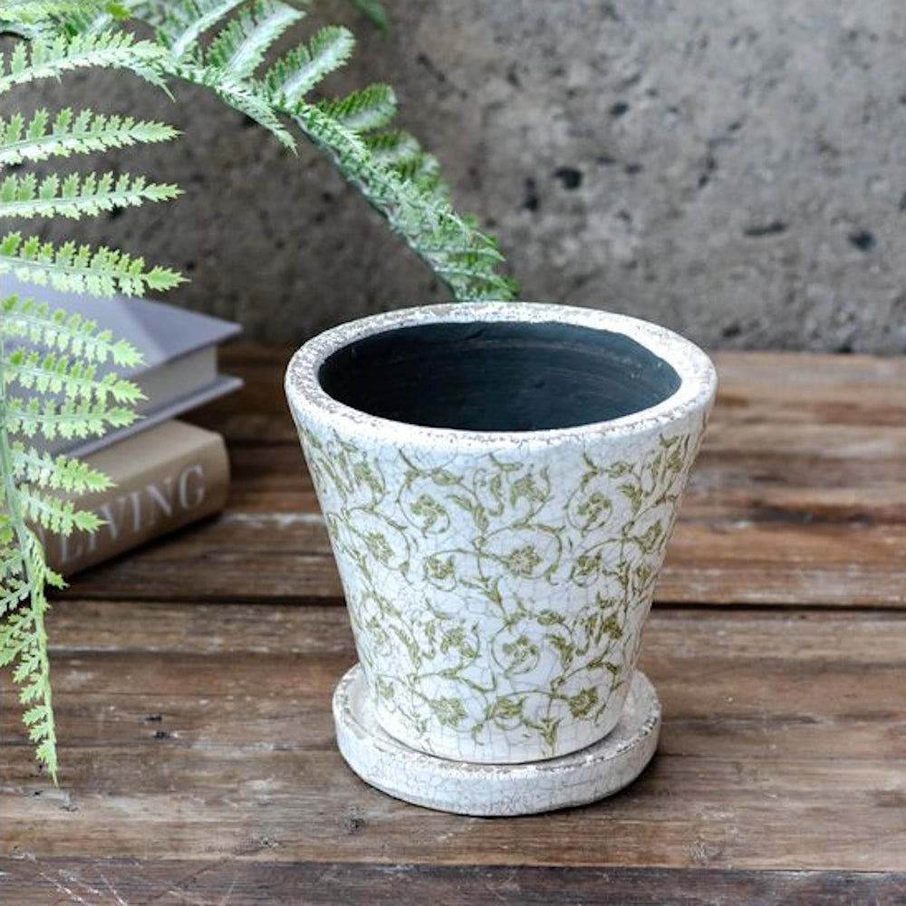 Antique-style white crackle glaze ceramic planter with green floral pattern and matching saucer on a wooden surface.