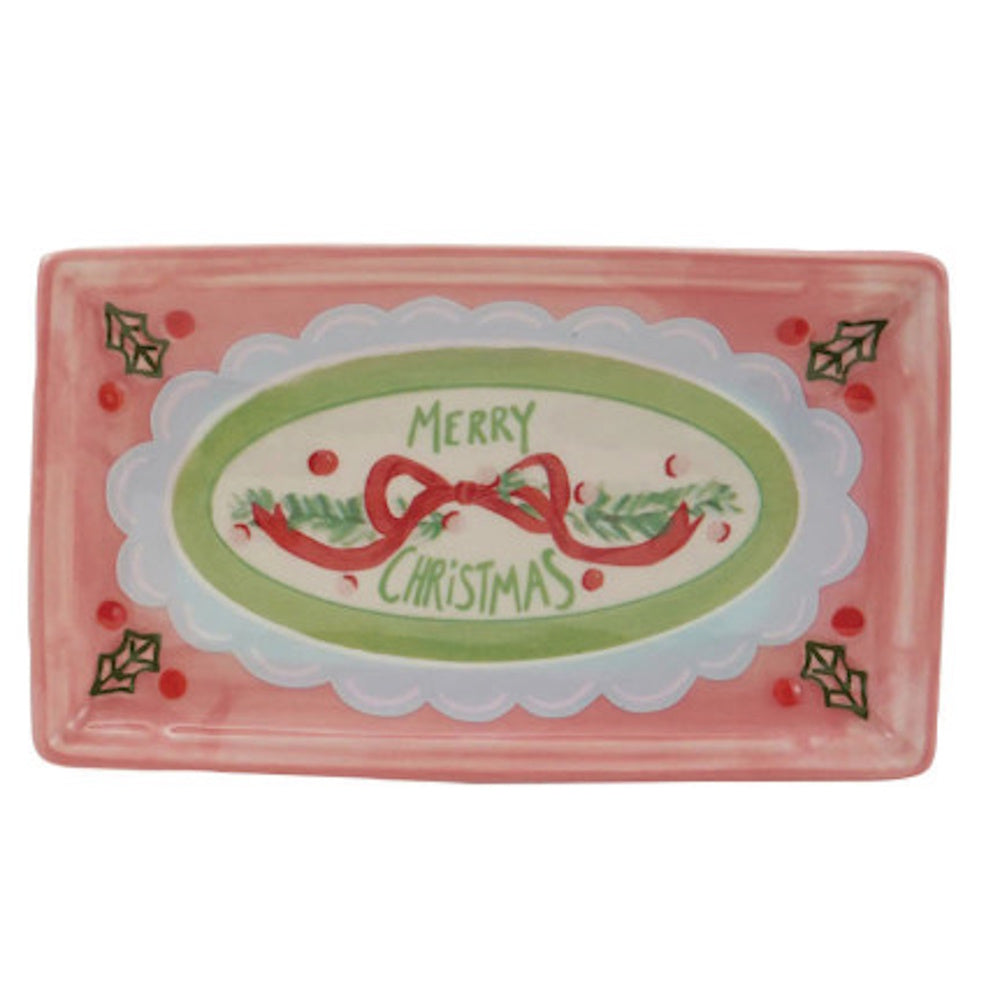 Rectangular pink stoneware tray featuring a green and blue centerpiece with a red ribbon garland and the phrase "MERRY CHRISTMAS".