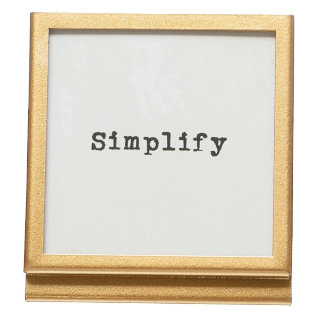 Square gold metal picture frame with glass insert featuring the word "Simplify" in black typewriter font on a white background.