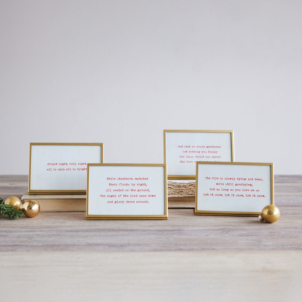 Small brass framed Christmas carol quotes displayed on a tabletop with holiday ornaments.