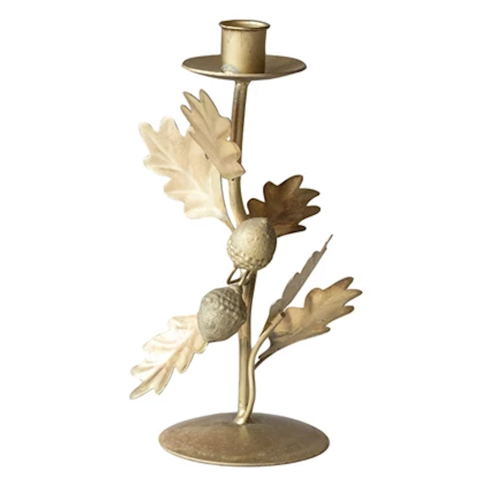 Gold-toned metal single taper candle holder with decorative oak leaves and acorns on a white background.