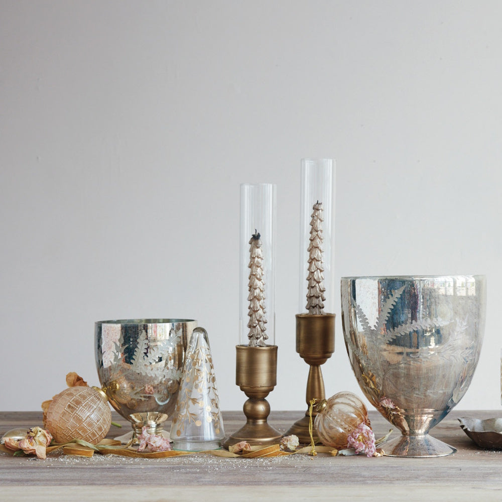 Brass candle holders with glass hurricanes and textured tree candles, arranged among silver glassware.