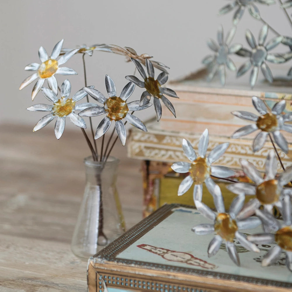 Close-up view of vintage-style metal daisy ornaments arranged in a glass flask next to vintage boxes.