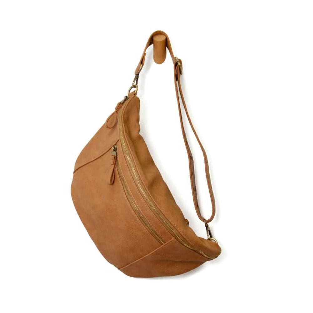 Tan leather crossbody sling bag with gold zippers and adjustable strap hanging on a wooden wall peg.