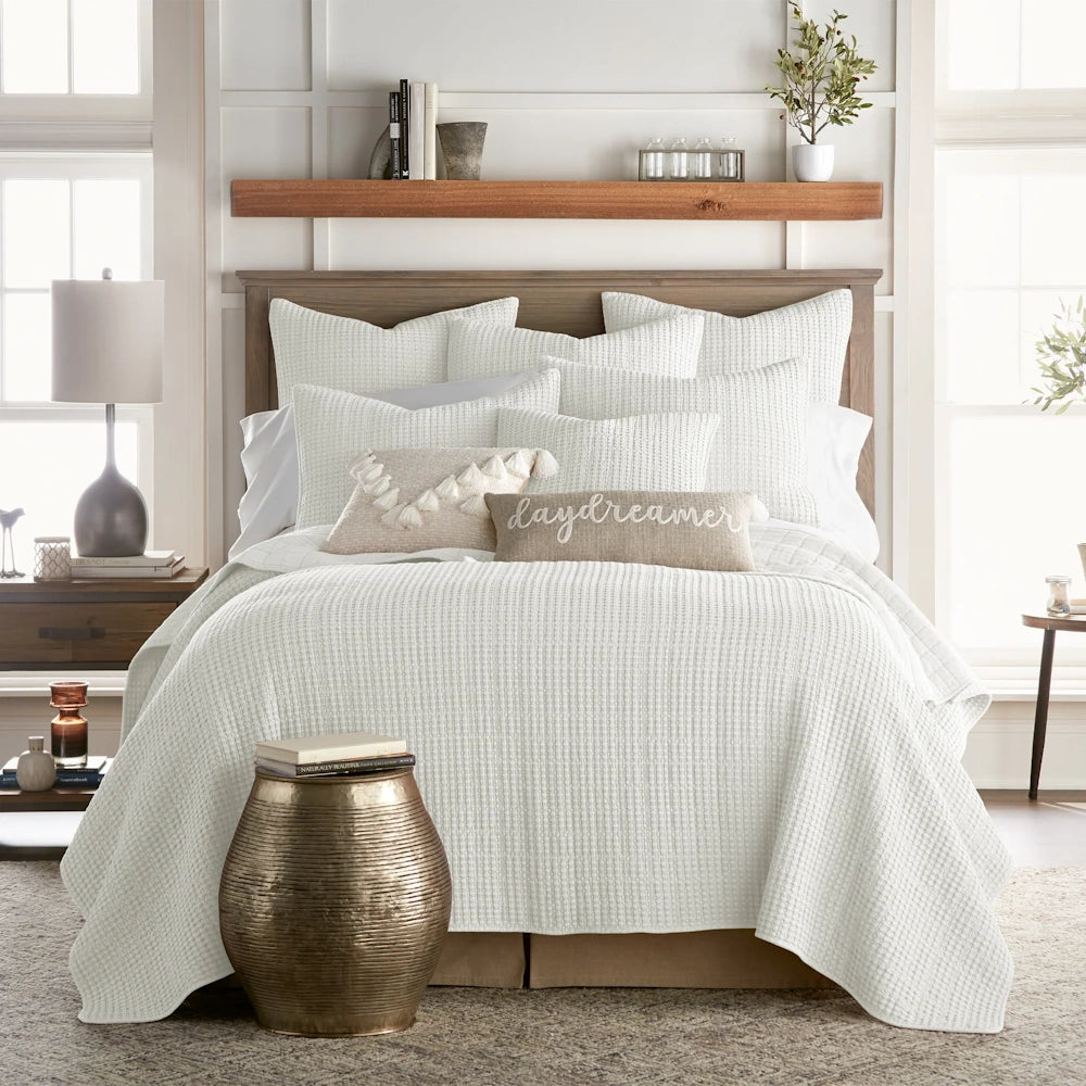 White waffle-weave quilt and matching pillows on a rustic wooden bed in a bright, modern farmhouse bedroom.