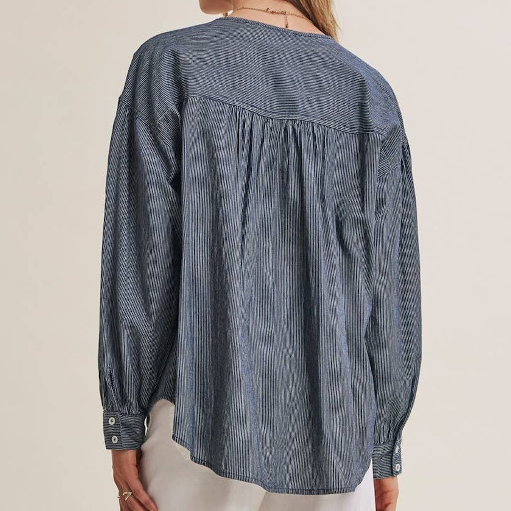 Back view of model wearing a mineral-washed, blue pinstripe chambray long-sleeve shirt with a back yoke.