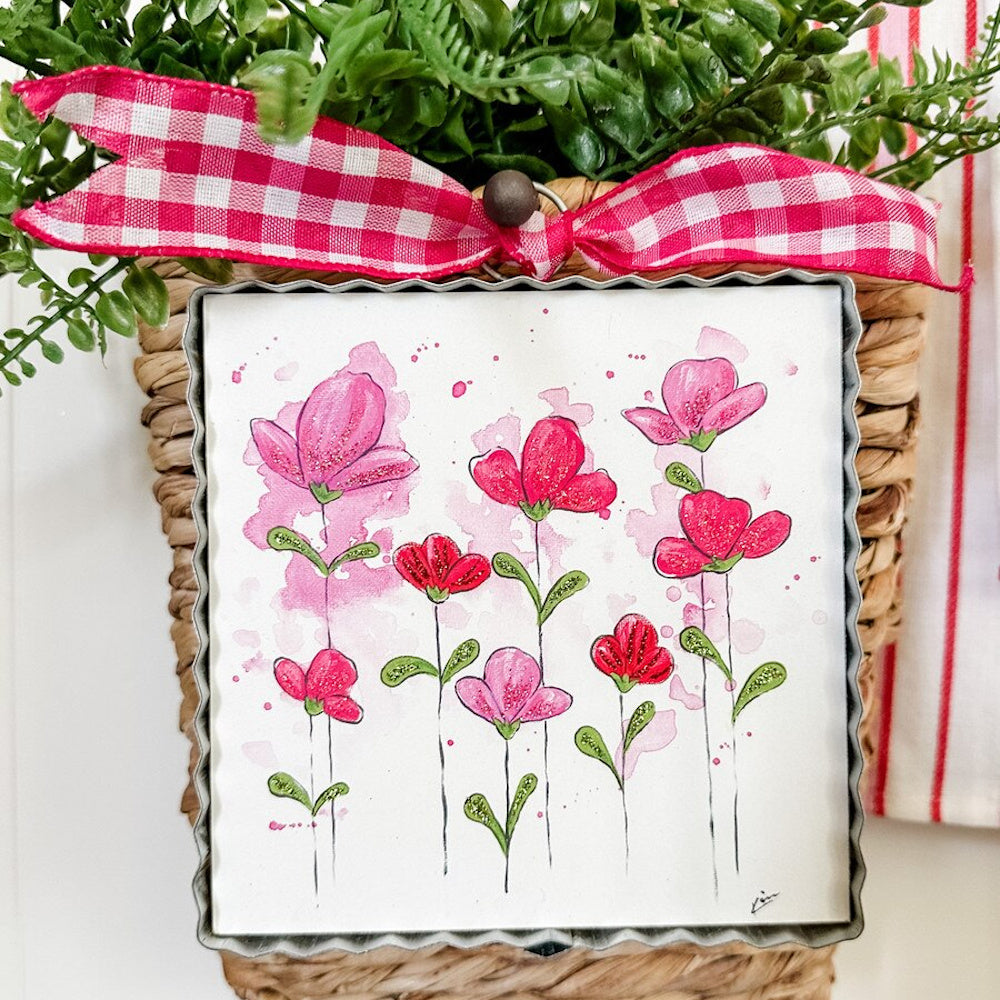 Whimsical watercolor pink flower art in a scalloped metal frame, decorated with a red gingham bow and green foliage.